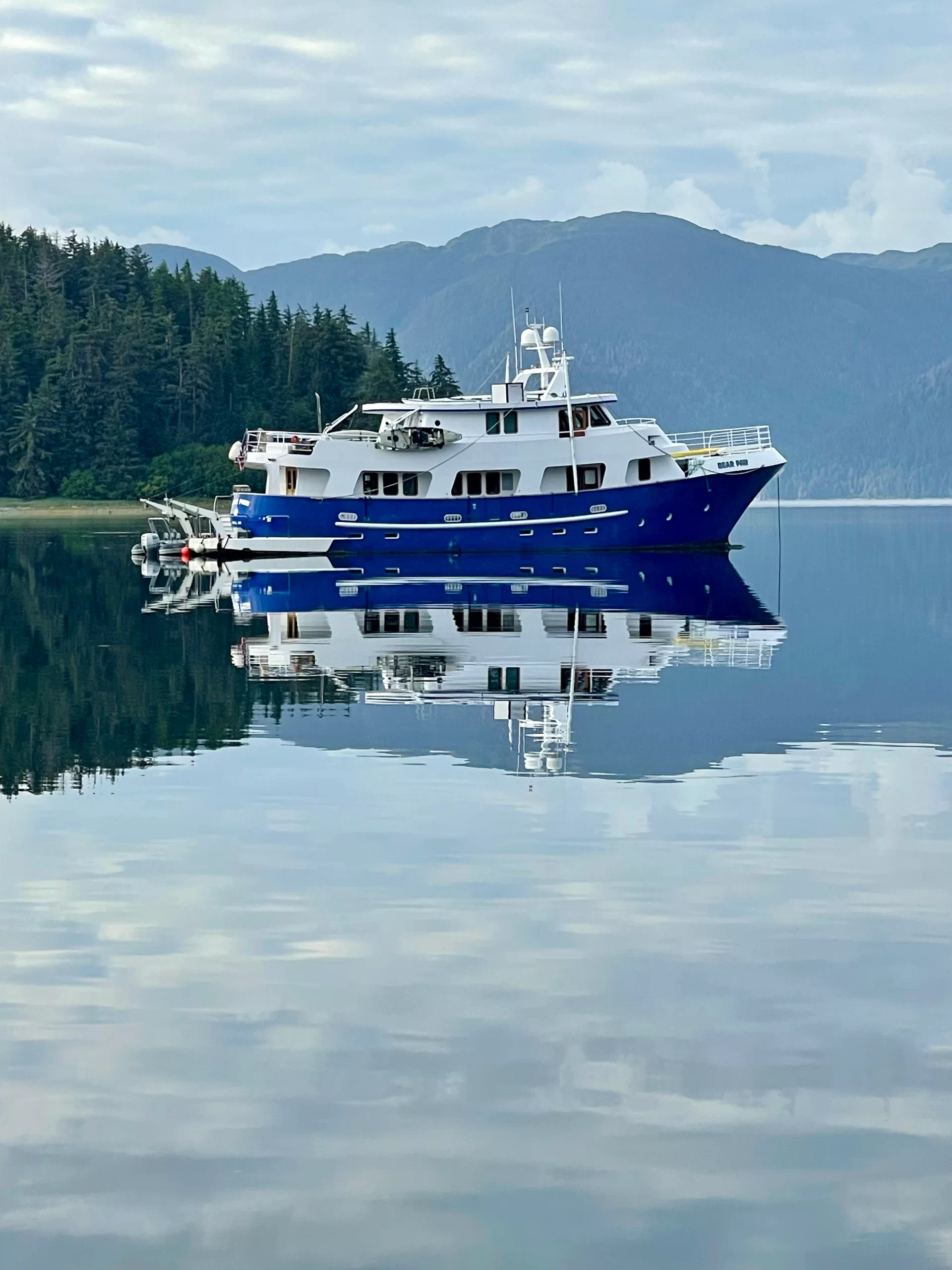 Luxury 90-foot motor yacht Bear Paw anchored on glass-calm water in a remote Alaskan bay.